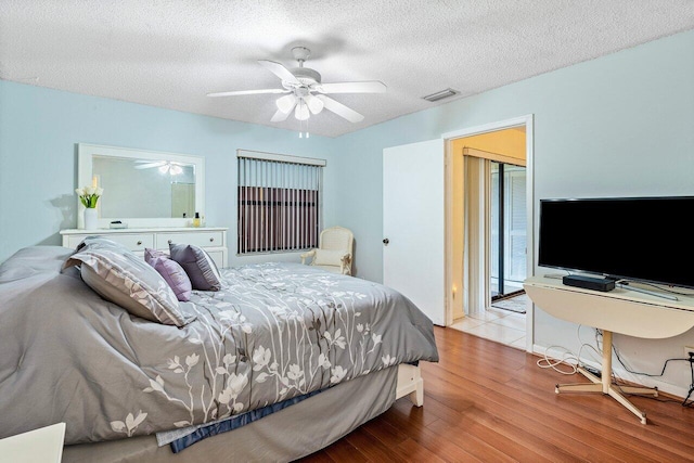 bedroom featuring a textured ceiling, visible vents, a ceiling fan, and wood finished floors