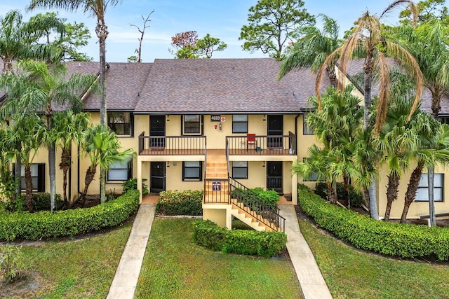 multi unit property with roof with shingles, stucco siding, a front yard, and stairs
