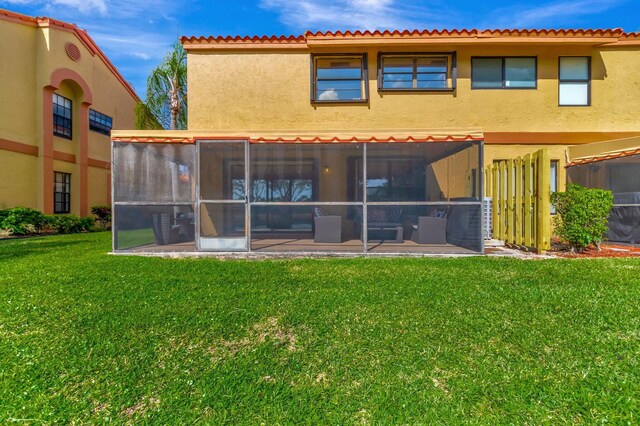 rear view of property featuring a lawn, a sunroom, and stucco siding