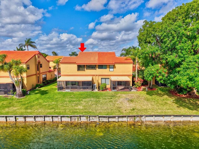 rear view of property with a tiled roof, a lawn, a sunroom, a water view, and stucco siding
