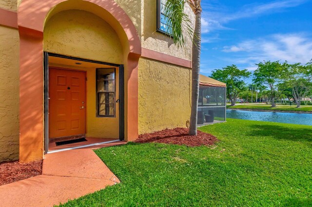 doorway to property featuring a water view, stucco siding, and a lawn