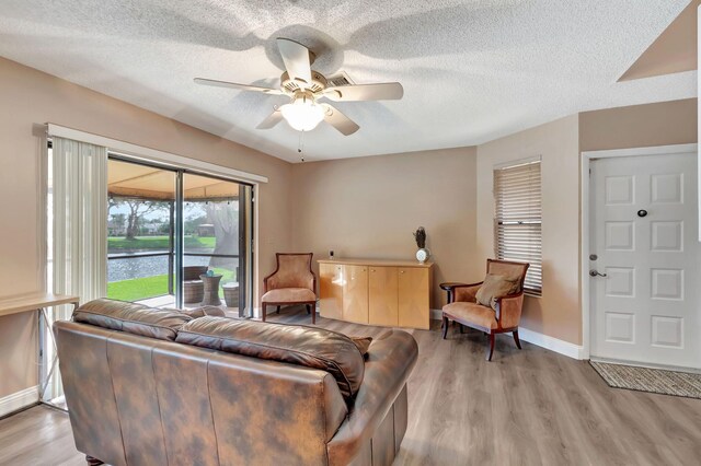 living room featuring light wood-style floors, baseboards, ceiling fan, and a textured ceiling