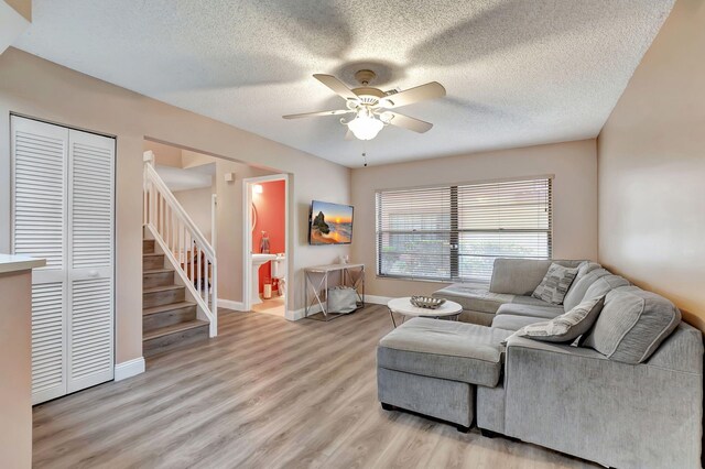 living room with a ceiling fan, baseboards, stairway, and light wood-type flooring