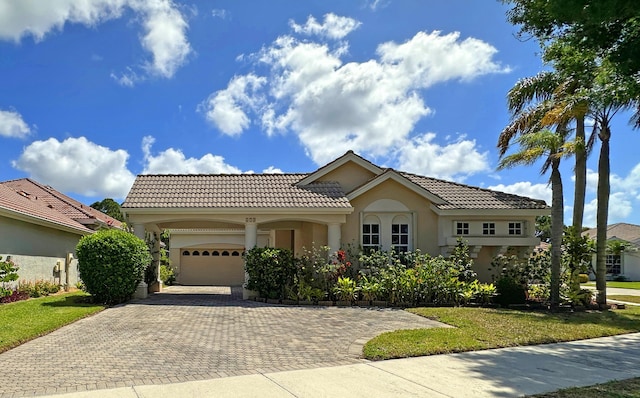 573 SW Saint Kitts St, Port Saint Lucie, FL 34953 - mediterranean / spanish-style house with an attached garage, decorative driveway, stucco siding, a tiled roof, and a front lawn