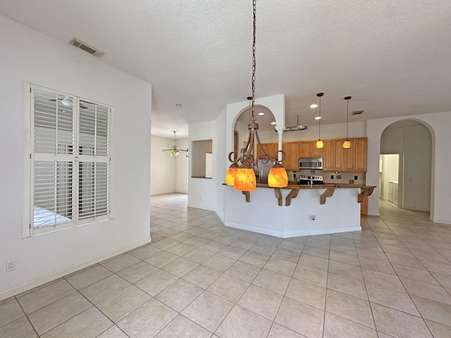 573 SW Saint Kitts St, Port Saint Lucie, FL 34953 - kitchen with stainless steel microwave, arched walkways, a breakfast bar area, light tile patterned floors, and a peninsula