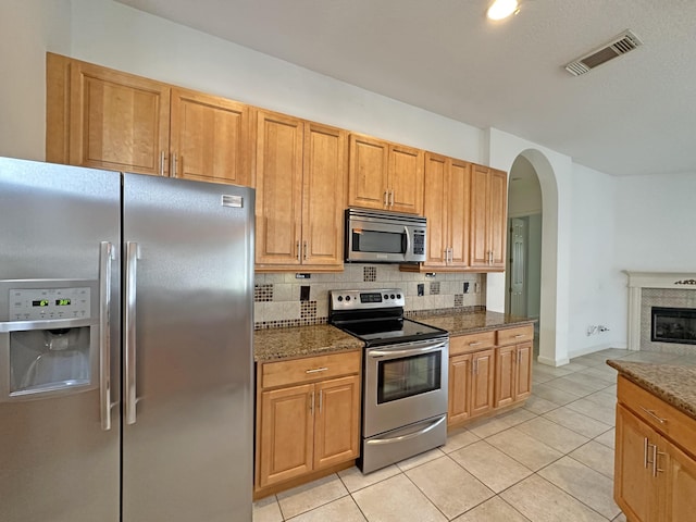 573 SW Saint Kitts St, Port Saint Lucie, FL 34953 - kitchen with stainless steel appliances, backsplash, arched walkways, light tile patterned flooring, and a glass covered fireplace