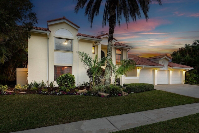 mediterranean / spanish house featuring a tile roof, a lawn, driveway, and a garage