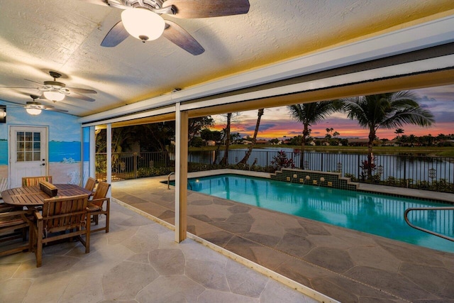 pool at dusk with a fenced in pool, a fenced backyard, a ceiling fan, and a water view
