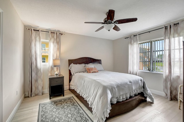 bedroom featuring light wood-type flooring, baseboards, ceiling fan, and a textured ceiling