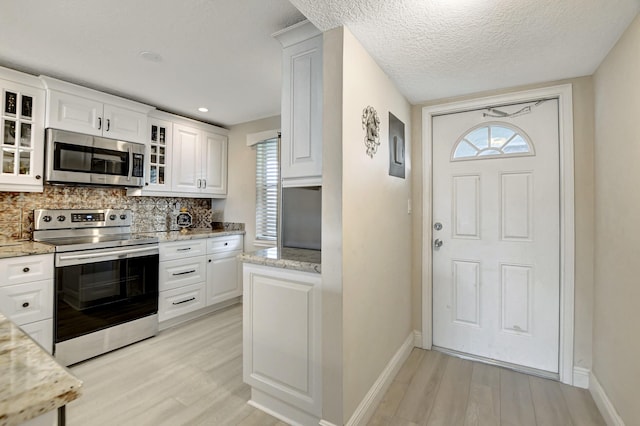 kitchen featuring stainless steel appliances, light wood finished floors, backsplash, white cabinetry, and baseboards