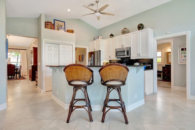kitchen with white cabinets, a breakfast bar area, stainless steel appliances, a ceiling fan, and light tile patterned floors