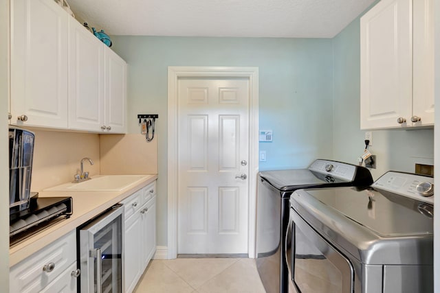 washroom with cabinet space, a sink, light tile patterned floors, beverage cooler, and washer and clothes dryer