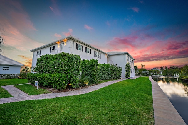 property exterior at dusk featuring stucco siding and a yard