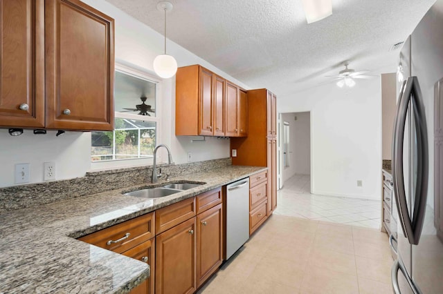 kitchen featuring brown cabinetry, ceiling fan, light stone counters, a sink, and stainless steel appliances