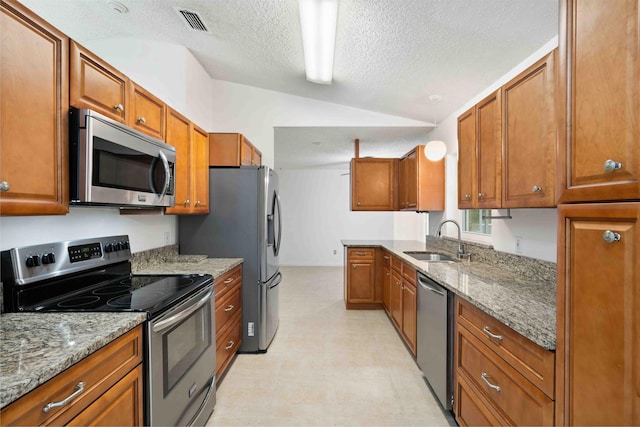 kitchen featuring appliances with stainless steel finishes, a sink, a textured ceiling, lofted ceiling, and visible vents