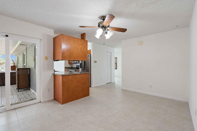 kitchen featuring a ceiling fan, baseboards, brown cabinetry, and stainless steel fridge