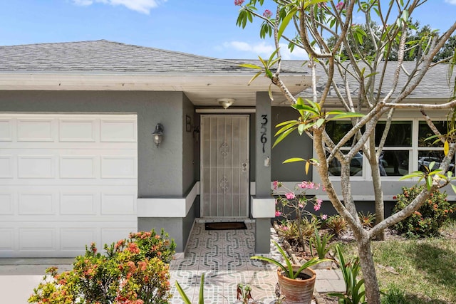 view of exterior entry featuring an attached garage, roof with shingles, and stucco siding