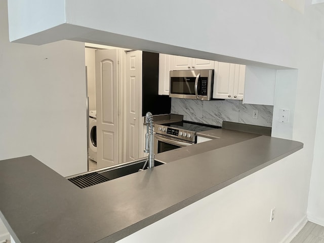 kitchen featuring white cabinets, dark countertops, appliances with stainless steel finishes, washer / dryer, and tasteful backsplash