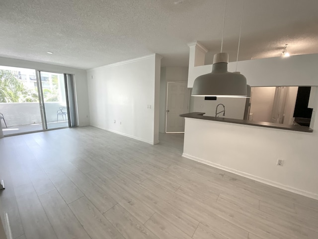 unfurnished living room featuring baseboards, a sink, a textured ceiling, and wood finished floors