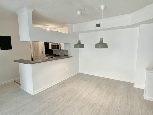 kitchen with a textured ceiling, visible vents, light wood-type flooring, stainless steel microwave, and a peninsula