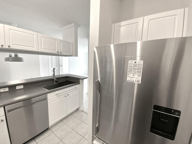 kitchen featuring dark countertops, appliances with stainless steel finishes, a sink, white cabinetry, and light tile patterned floors