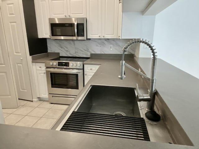 kitchen featuring backsplash, a sink, light tile patterned flooring, stainless steel appliances, and white cabinetry