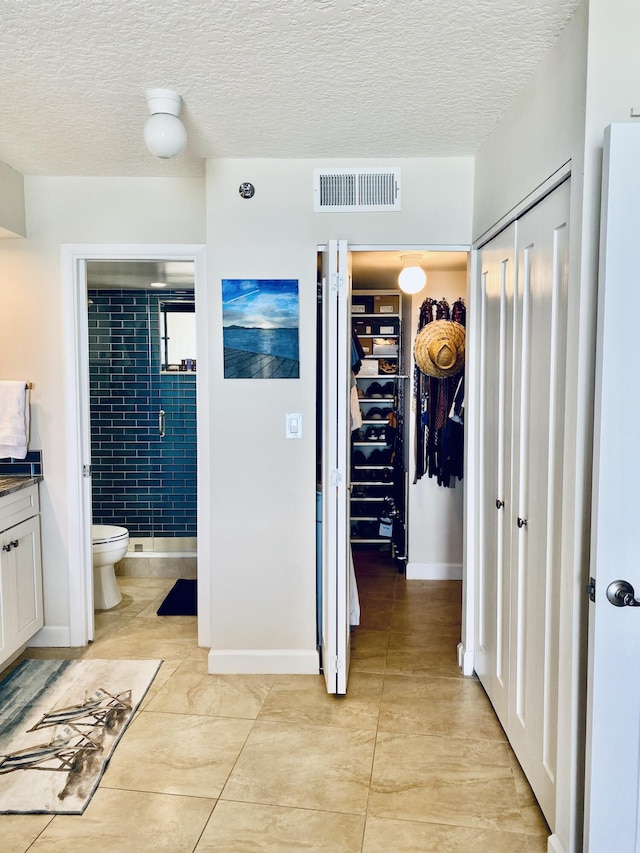 full bathroom featuring a walk in closet, visible vents, tile patterned flooring, a shower stall, and toilet