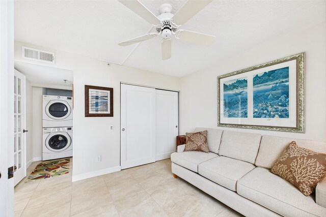 living area featuring visible vents, light tile patterned flooring, stacked washer / dryer, baseboards, and ceiling fan