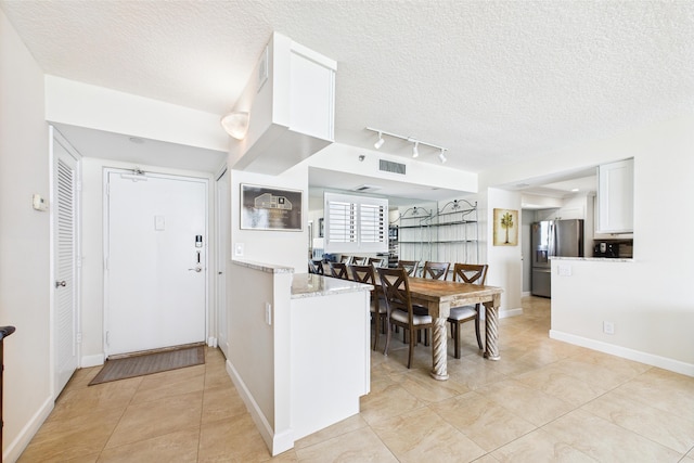 kitchen with stainless steel fridge, a textured ceiling, light tile patterned flooring, and visible vents