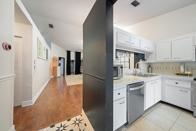 kitchen featuring a sink, stainless steel appliances, visible vents, white cabinetry, and tile countertops