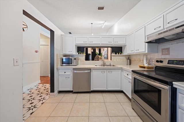 kitchen with under cabinet range hood, appliances with stainless steel finishes, light countertops, a sink, and white cabinetry