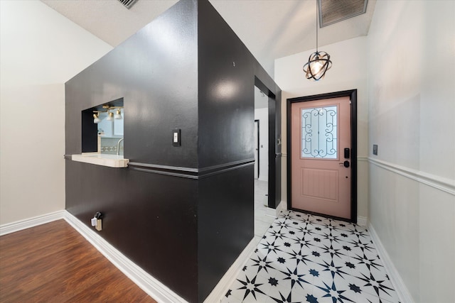 foyer entrance with light floors, visible vents, vaulted ceiling, and baseboards