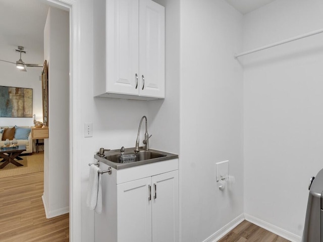 washroom with baseboards, a sink, light wood finished floors, and cabinet space