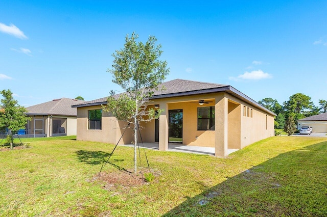 6056 NW Regent St, Port Saint Lucie, FL 34983 - rear view of property featuring a ceiling fan, roof with shingles, a lawn, a patio, and stucco siding