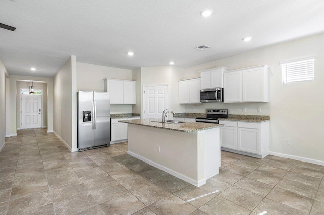 6056 NW Regent St, Port Saint Lucie, FL 34983 - kitchen with visible vents, an island with sink, light stone counters, a sink, and stainless steel appliances