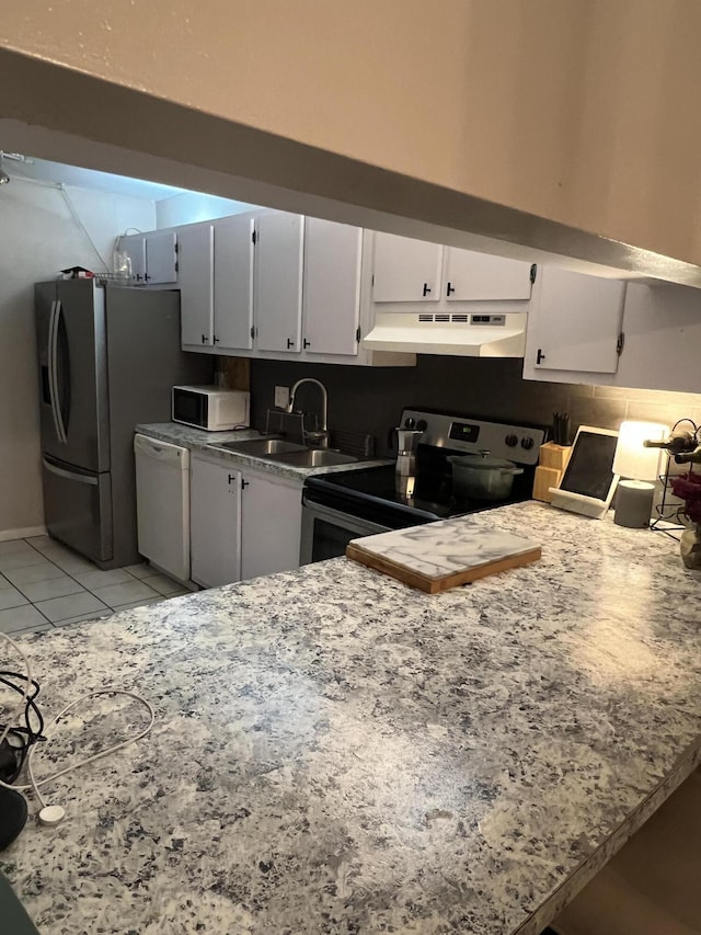 kitchen with a sink, under cabinet range hood, light tile patterned floors, a peninsula, and appliances with stainless steel finishes