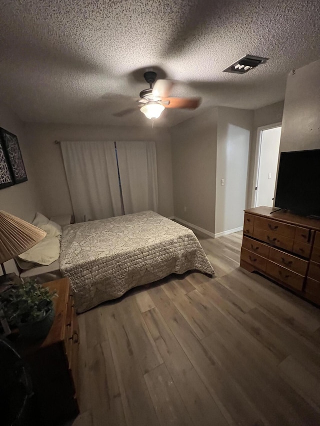 bedroom featuring a textured ceiling, visible vents, wood finished floors, and baseboards