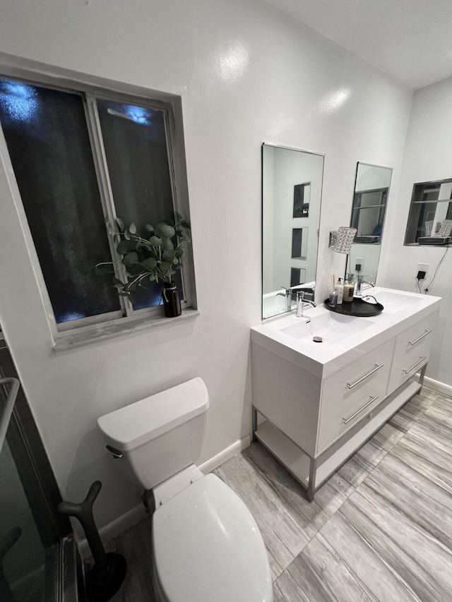 full bathroom featuring a sink, double vanity, baseboards, toilet, and wood finished floors