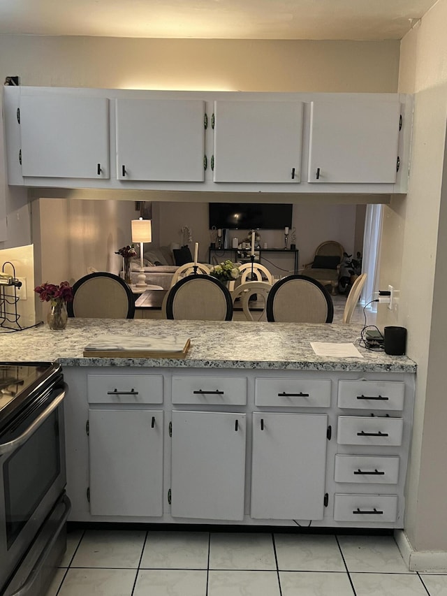 kitchen featuring light tile patterned floors, stainless steel range with electric stovetop, and white cabinets