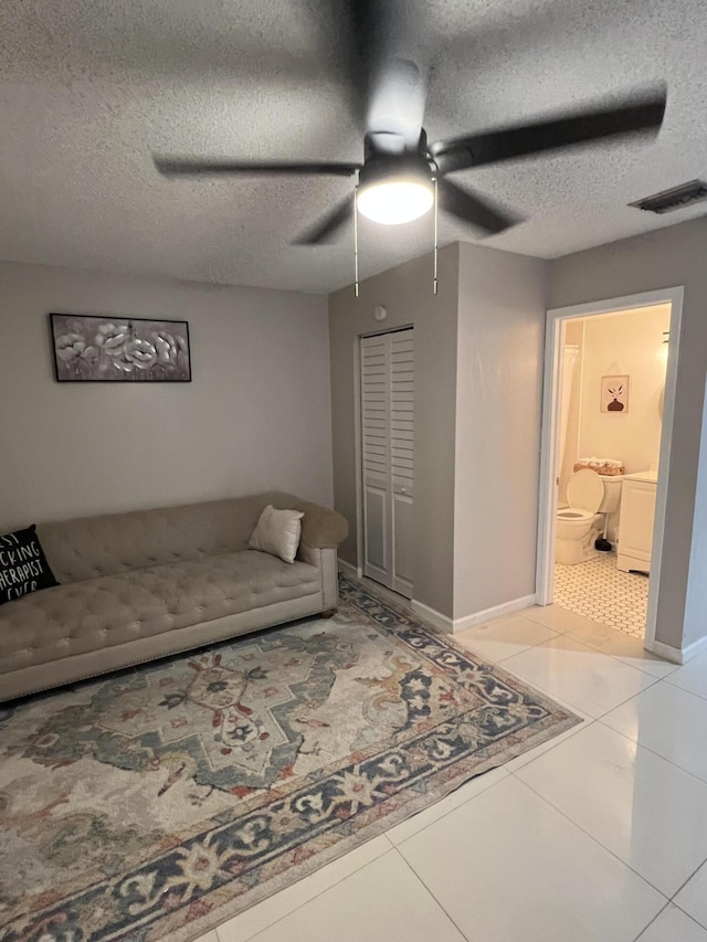 living room featuring light tile patterned floors, baseboards, visible vents, a ceiling fan, and a textured ceiling
