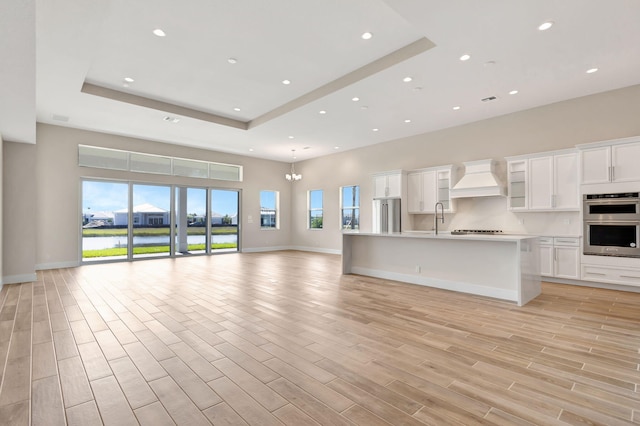 unfurnished living room featuring a raised ceiling, baseboards, light wood-type flooring, and recessed lighting