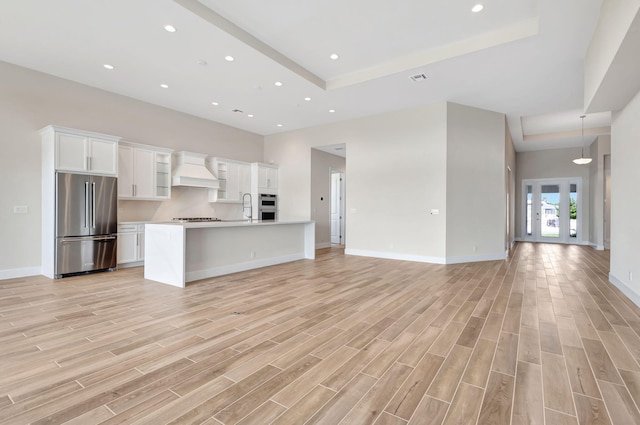 kitchen featuring high end fridge, a sink, white cabinetry, open floor plan, and custom exhaust hood