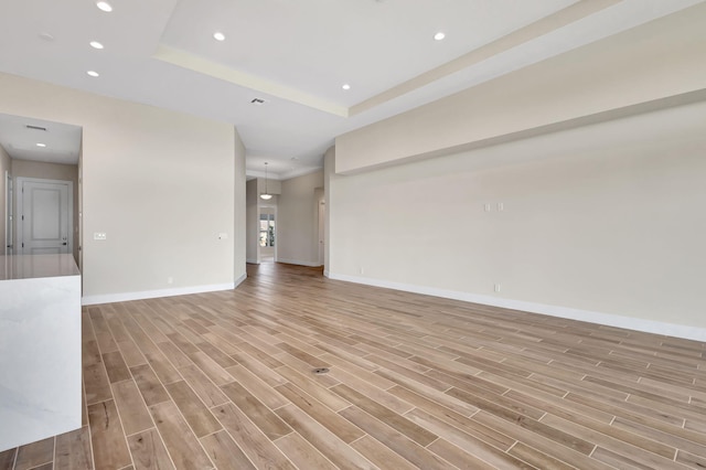 unfurnished room featuring recessed lighting, baseboards, a raised ceiling, and light wood-type flooring