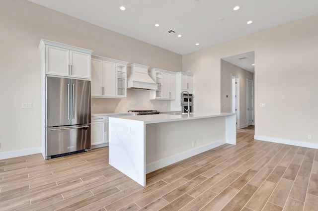 kitchen featuring light countertops, white cabinets, freestanding refrigerator, custom exhaust hood, and light wood-style floors