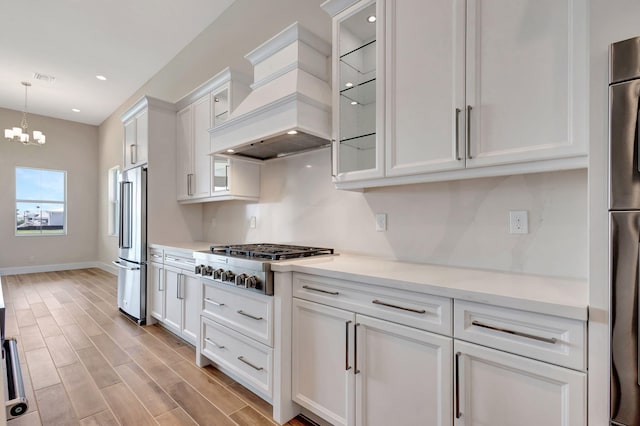 kitchen featuring pendant lighting, appliances with stainless steel finishes, light countertops, premium range hood, and white cabinets