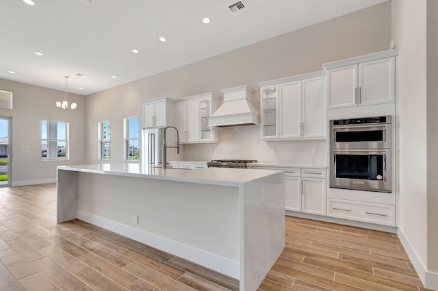 kitchen with stainless steel double oven, a sink, light countertops, premium range hood, and visible vents
