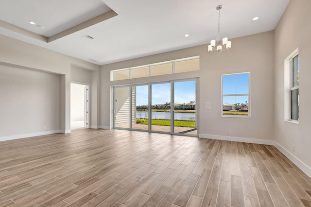 empty room with a notable chandelier, light wood finished floors, baseboards, a water view, and visible vents