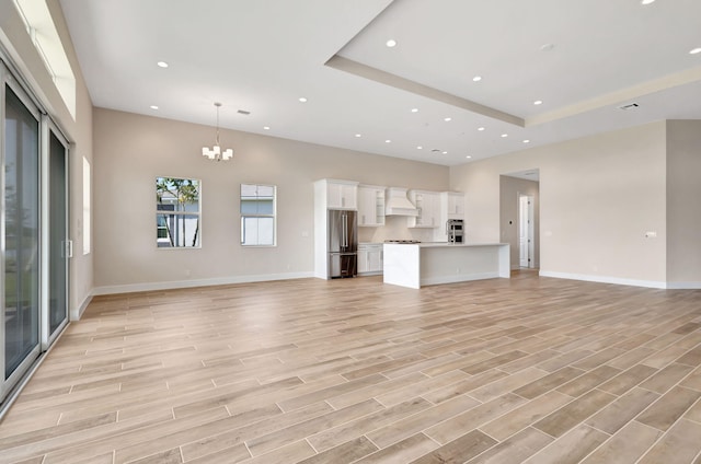 unfurnished living room featuring light wood-style floors, a towering ceiling, baseboards, an inviting chandelier, and recessed lighting