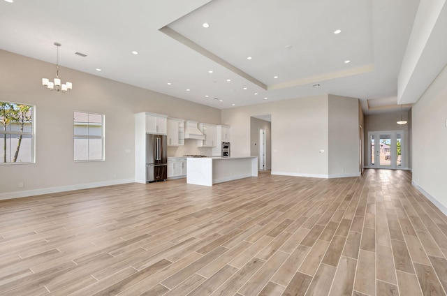 unfurnished living room with recessed lighting, a tray ceiling, and baseboards