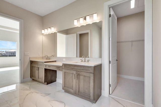 bathroom with a sink, baseboards, double vanity, and a spacious closet